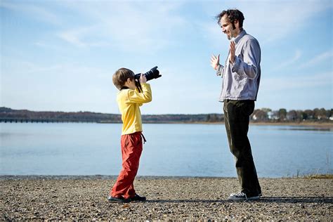 Child On Beach Takes Photo Of His Father With Camera By Stocksy