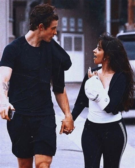 A Man And Woman Are Walking Down The Street Holding Hands While Talking To Each Other