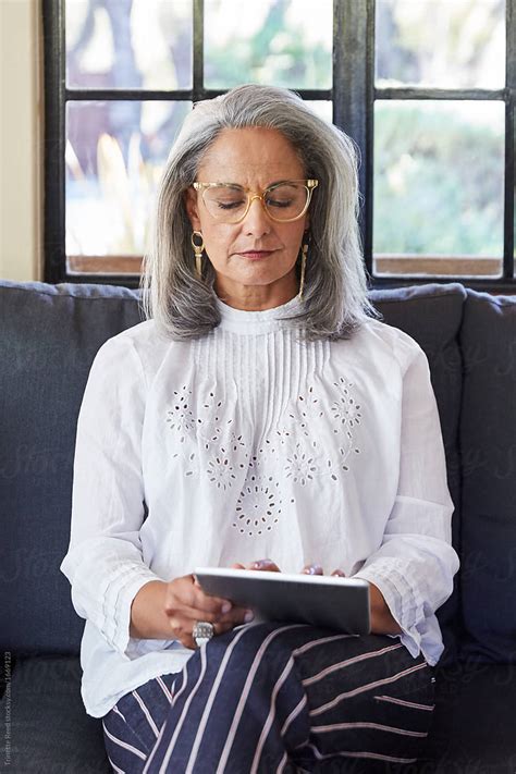 Mature Woman With Grey Hair Using A Digital Tablet In Living Room By