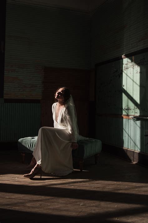 A Woman Sitting On Top Of A Bed In A Room With Sunlight Coming Through