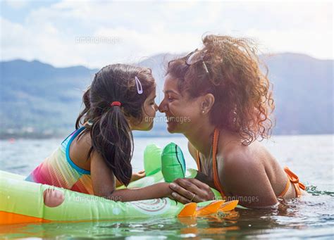 Mother Rubbing Noses With Daughter On Inflatable Frog In Lake