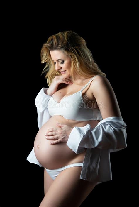 Beautiful Blonde Pregnant Woman In White Clothes On A Black Background