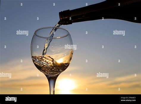 White Wine Pouring From A Bottle Into The Glass On Sunset Sky