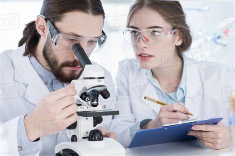 Two Coworkers Chemists Working With Microscope And Taking Notes In