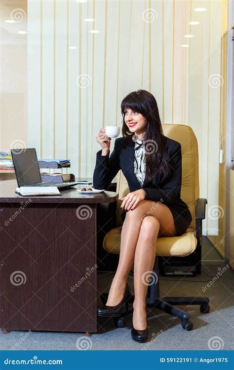 Beautiful Woman In A Short Skirt Drinking Coffee In Office Stock Photo