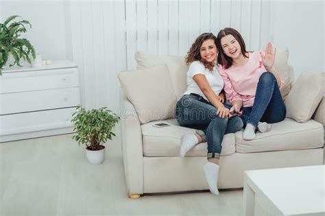 Two Amazing Girls Sitting On The Sofa Hugging One Another Smiling At