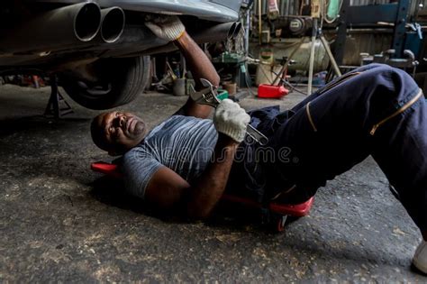 Mechanic Lying Down And Working Under Car At Auto Service Garage