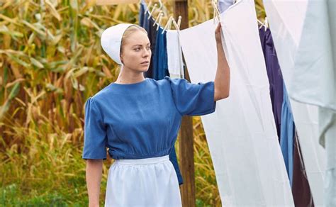 A Woman In A Blue Dress Hanging Out Clothes On A Line With Corn Stalks