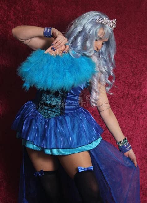 Woman With Blue Hair And Blue Corset Dress Holding Blue Fan On Red Velvet Background Stock Image