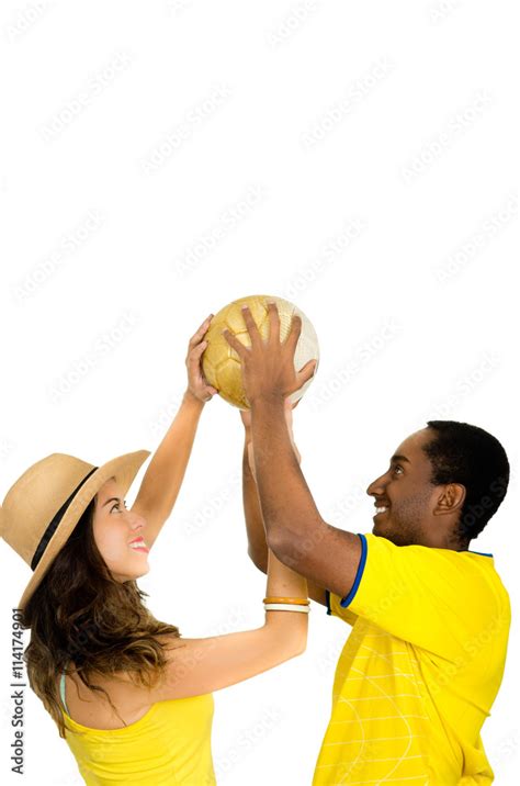 Charming Interracial Couple Wearing Yellow Football Shirts Holding Ball Up In Air Between Each