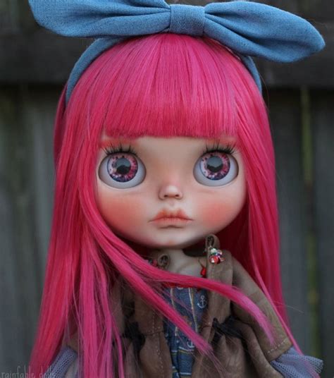 A Doll With Pink Hair And Big Eyes Wearing A Blue Bow Headband