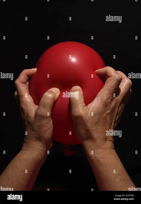 A Womans Hands Aggressively Squeeze An Inflated Red Balloon Against A