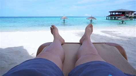 Tourist Legs Bare Feet Sitting On Golden Sand Beach Bench Point Out To