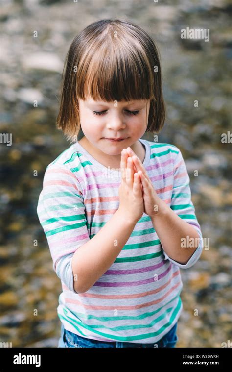 Little Girl Praying With Eyes Closed On The Shore Of A Mountain Stream