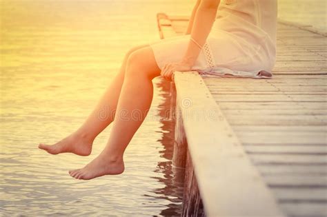 Female Sitting On Pier At Sunset Close Up Of Legs Hanging Into Stock