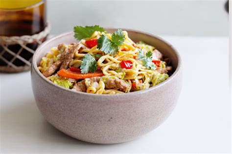A Bowl Filled With Noodles Meat And Veggies Next To A Bottle Of Oil
