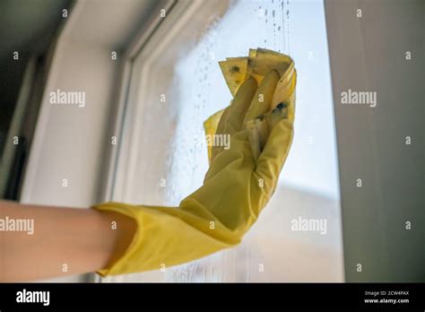 female hand in yellow gloves cleaning window pane with rag and spray detergent cleaning concept