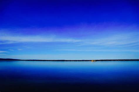 A Deep Blue Lake And Clear Sky Separated By A Dark Green Shoreline On