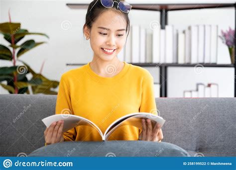 Happy Young Asian Woman Reading On The Sofa In The Living Room Stock