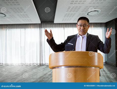 Businessman On Podium Speaking At Conference With Windows Stock Image