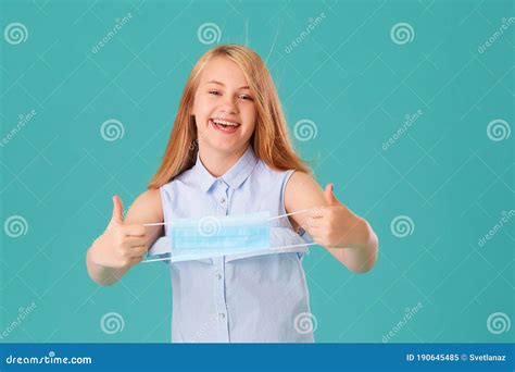 A Young Girl Takes Off Her Mask On A Turquoise Background She Is