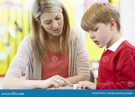 Insegnante Helping Male Pupil Con Lettura Allo Scrittorio Fotografia