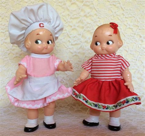 Two Dolls Are Standing Next To Each Other On A White Surface One Is