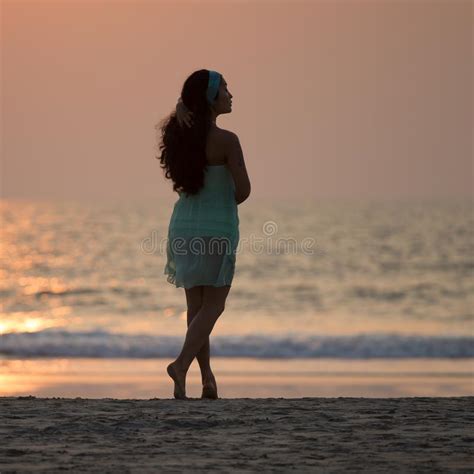 Silhouette Of A Beautiful Girl Standing On The Beach At Sunset Stock