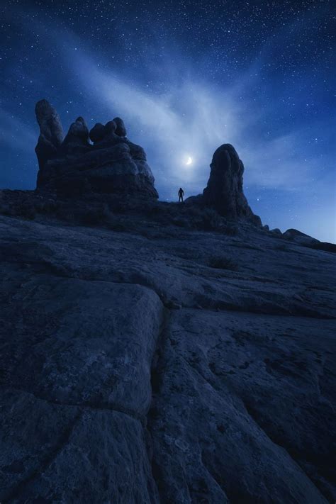 A Person Standing On Top Of A Rocky Hill Under A Night Sky