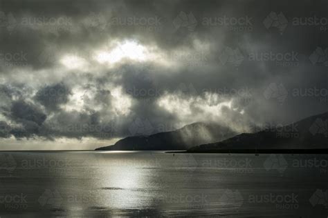 Image Of Sun Shining Through The Clouds Onto Ocean And Mountain