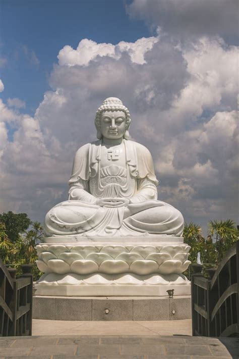 The Solemn White Statue Of Buddha Sitting On A High Pedestal Behind Is