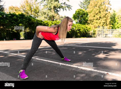 A Fit Female Runner Stops To Stretch In An Urban Park Setting Stock