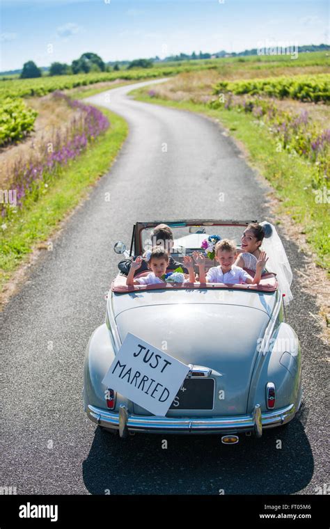 A Newlywed Couple Is Driving A Retro Car On A Country Road With Their