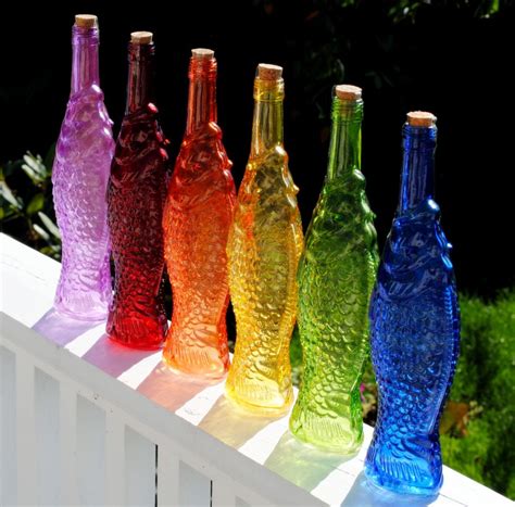 Seven Colorful Glass Bottles Lined Up On A White Fence
