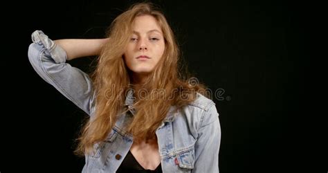 Cute Girl With Long Blonde Hair And A Denim Jacket Posing On A Black