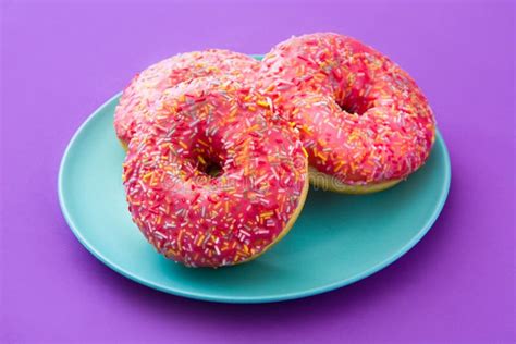 Pink Frosted Donut With Colorful Sprinkles On Violet Background Stock