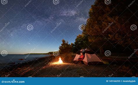 Woman Having A Rest At Night Camping Near Tourist Tent Campfire On Sea
