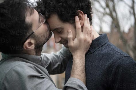 Bearded Man Kissing On Forehead Of Male Friend Outdoors Stock Photo