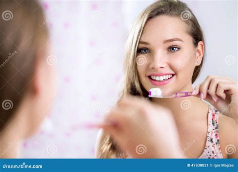 Pretty Female Looking In Mirror While Brushing Teeth Stock Image