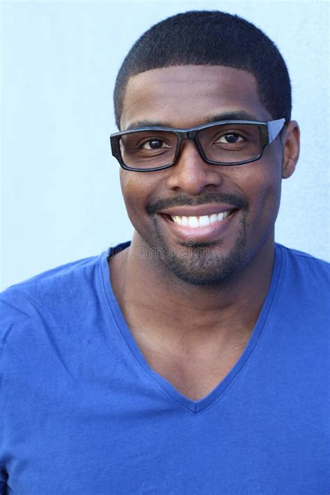 Close Up Smiling Young Black Man Wearing Eyeglasses Looking At The Camera Against Blue Wall