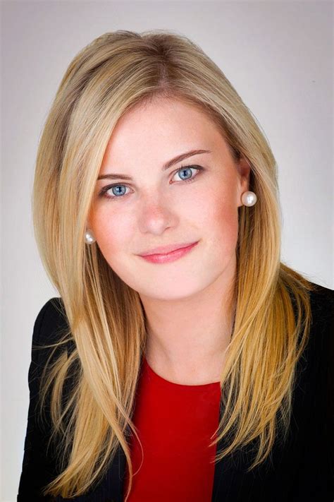 A Woman With Blonde Hair And Blue Eyes Wearing A Black Blazer Red Shirt And Pearl Earrings