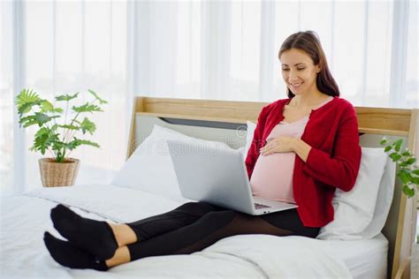 Pregnant Woman Sitting On Bed And Using Laptop With Smile And Happiness