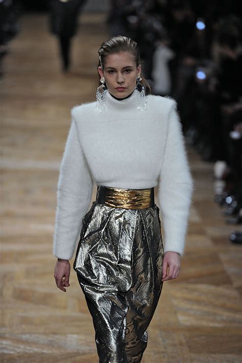 A Model Walks Down The Runway Wearing Metallic Pants And A White