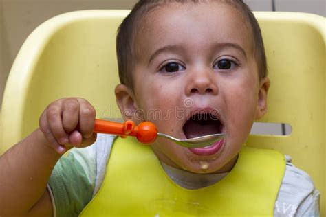 Little Baby Eats With A Spoon Soup Plate He Sits On A Children`s Chair