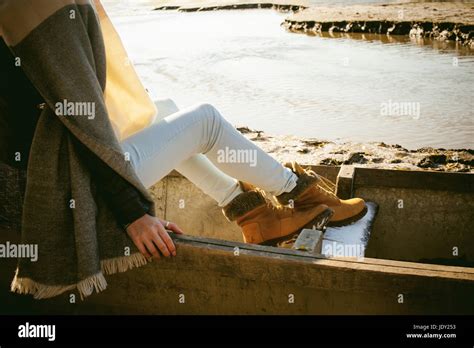 slim girl s legs in blue jeans and brown boots girl sat on the upturned boat on the shore