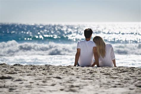 Reflecting On Their Love A Young Couple Sitting Together On The Beach And Admiring The