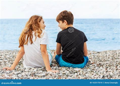 couple of beautiful teens first love guy hugs a girl sitting on the pebble beach next to each