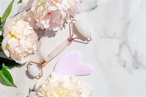 Gua Sha Massager And Face Roller On White Marble Background With Peony Flowers Massage Tools