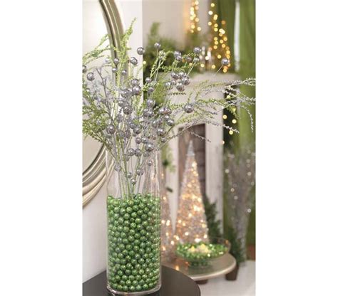 A Vase Filled With Lots Of Green Beads And Silver Flowers On Top Of A Table