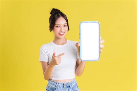 Premium Photo Young Asian Woman Holding Phone With Cheerful Face On Yellow Background